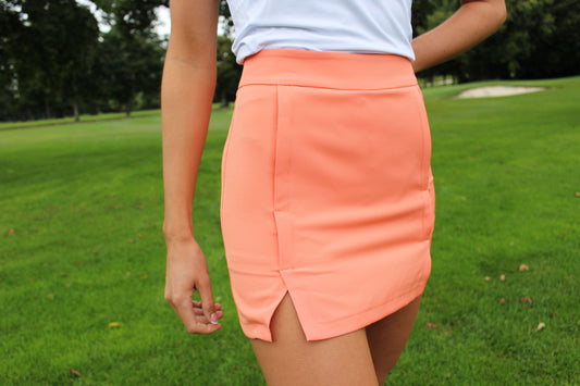 AWGO Golf Coral Skort on female golfer Women's high-waisted golf skort in coral Performance golf skirt with stretchy fabric Close-up of pocketed golf skort in coral Female golfer wearing AWGO Golf Coral Skort Stylish women's golf apparel in coral Sporty golf outfit with high-waisted skort Golf skort with convenient pockets AWGO Golf Coral Skort for female golfers Coral golf skort for performance and style