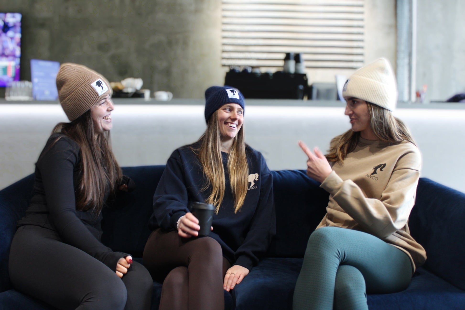 women in cafe drinking coffee in beanie hats and sweatshirts